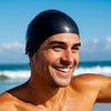 Hombre sonriendo usando una gorra de silicona negra para nadar al aire libre cerca del océano.