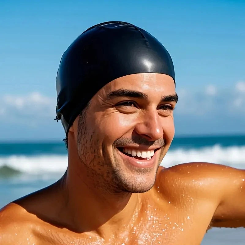 Hombre sonriendo usando una gorra de silicona negra para nadar al aire libre cerca del océano.