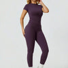 Eine Frau modelliert ein zweiteiliges Yoga-Set mit lila, hoch taillierter Leggings und einem kurzen Oberteil.
