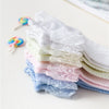 Une pile de chaussettes à volants en dentelle blanches, roses et bleues pour filles avec des élastiques colorés.