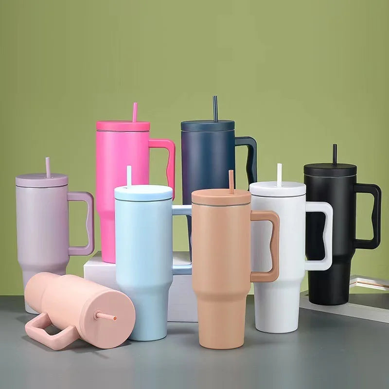 Collection de tasses isothermes en acier inoxydable de différentes couleurs avec paille, présentées sur une surface grise.
