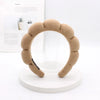 A beige sponge terry cloth headband for hair styling displayed on a white circular stand.