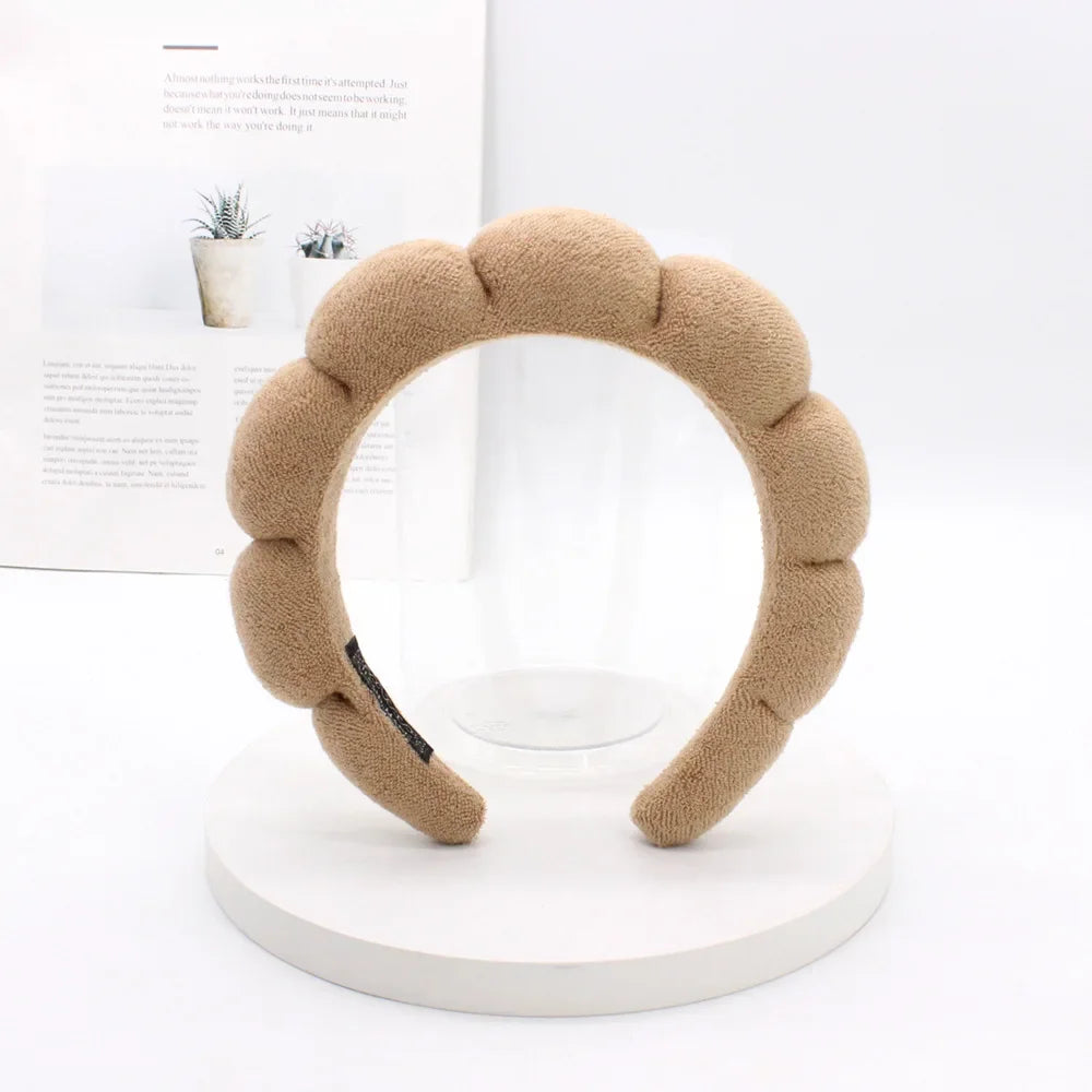 A beige sponge terry cloth headband for hair styling displayed on a white circular stand.