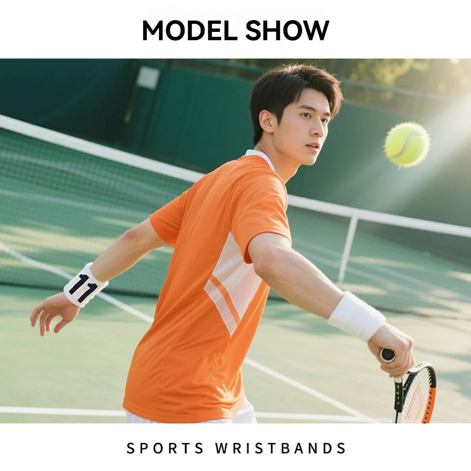 Un jeune homme en chemise orange joue au tennis, portant des bracelets blancs et tenant une raquette.