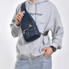 A man wearing a gray hoodie holds a dark blue leather crossbody bag with a gold buckle.