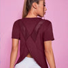 A woman wearing a maroon breathable summer yoga and fitness t-shirt with a crisscross back design.