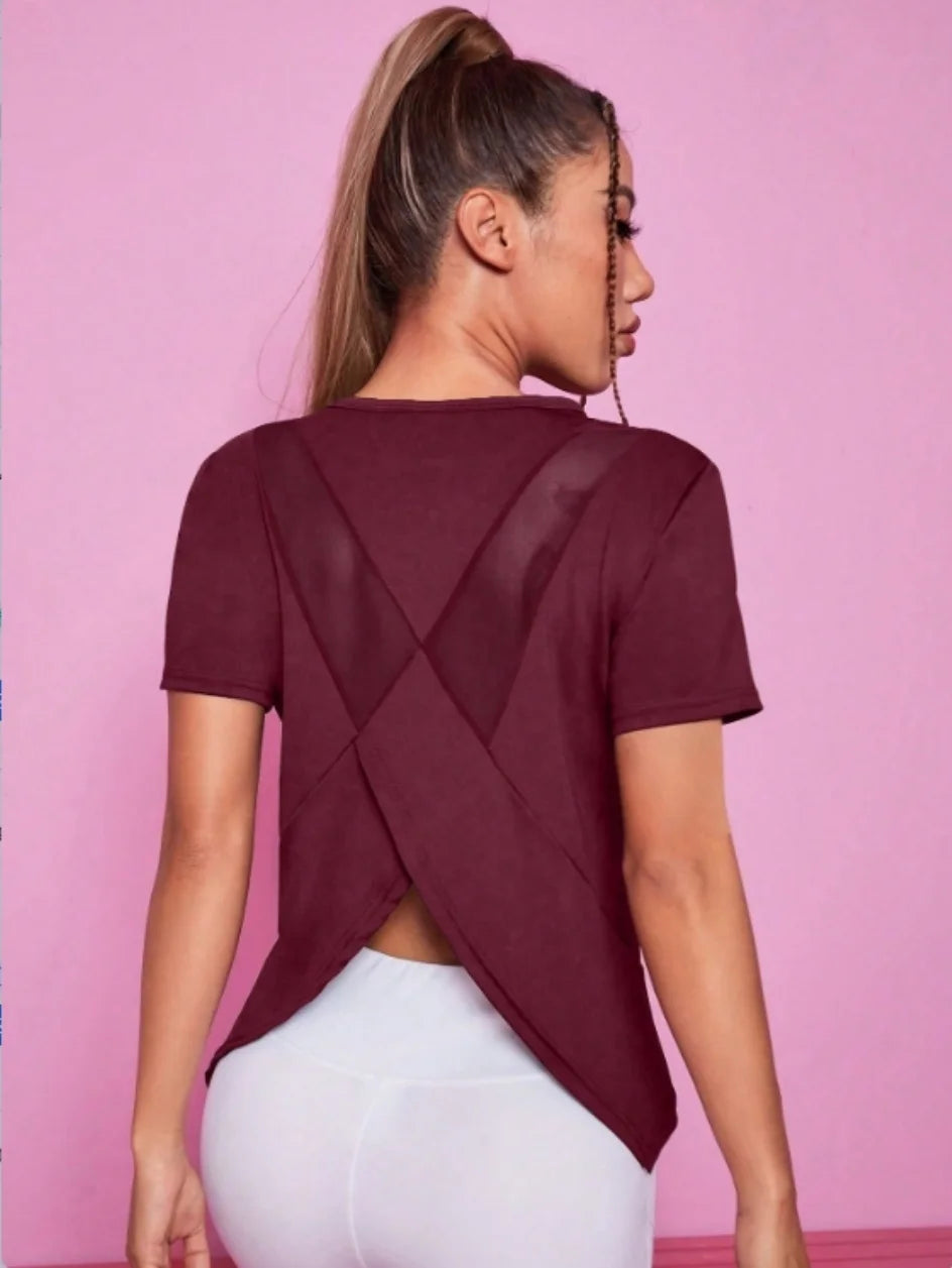 A woman wearing a maroon breathable summer yoga and fitness t-shirt with a crisscross back design.