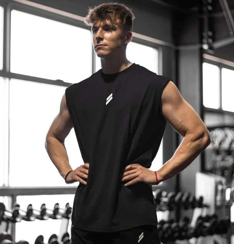 Muskulöser Mann in einem schwarzen Fitness-Tanktop steht in einem Fitnessstudio.