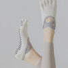 A close-up of a person's foot wearing white five-finger yoga and fitness socks with gray accents.
