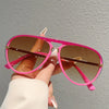 A hand holds a pair of pink gradient sunglasses with gold accents against a gray background.