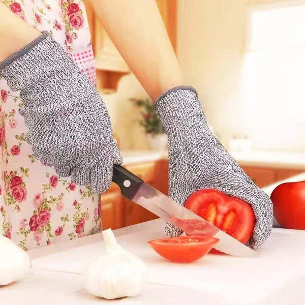 A hand wearing knitted protection gloves is holding a knife over fresh produce on a cutting board.