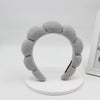 A gray sponge terry cloth headband for hair styling displayed on a white circular stand.