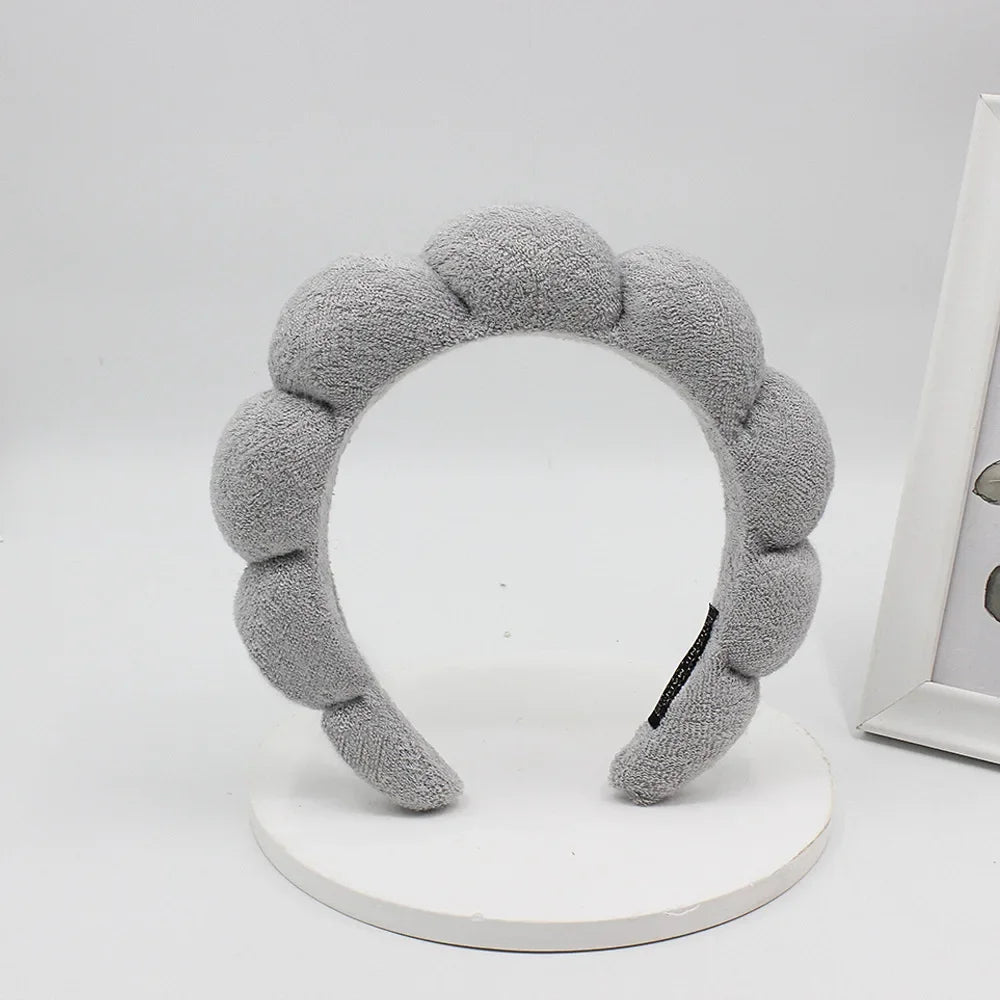 A gray sponge terry cloth headband for hair styling displayed on a white circular stand.