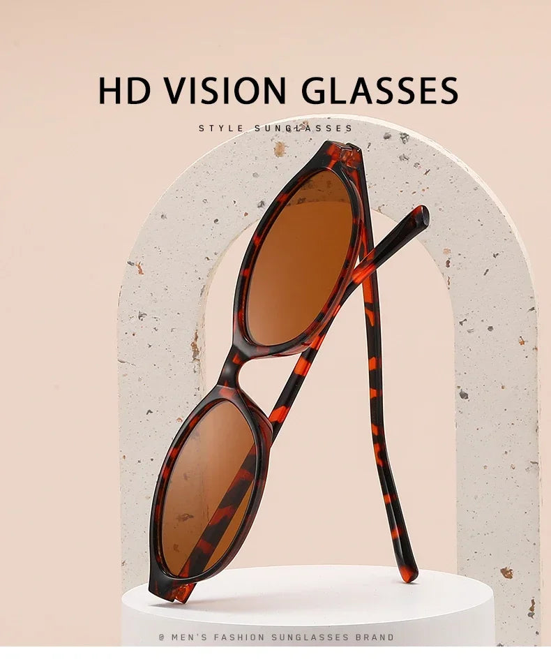 A pair of tortoiseshell patterned sunglasses with an oval frame displayed against a light background.