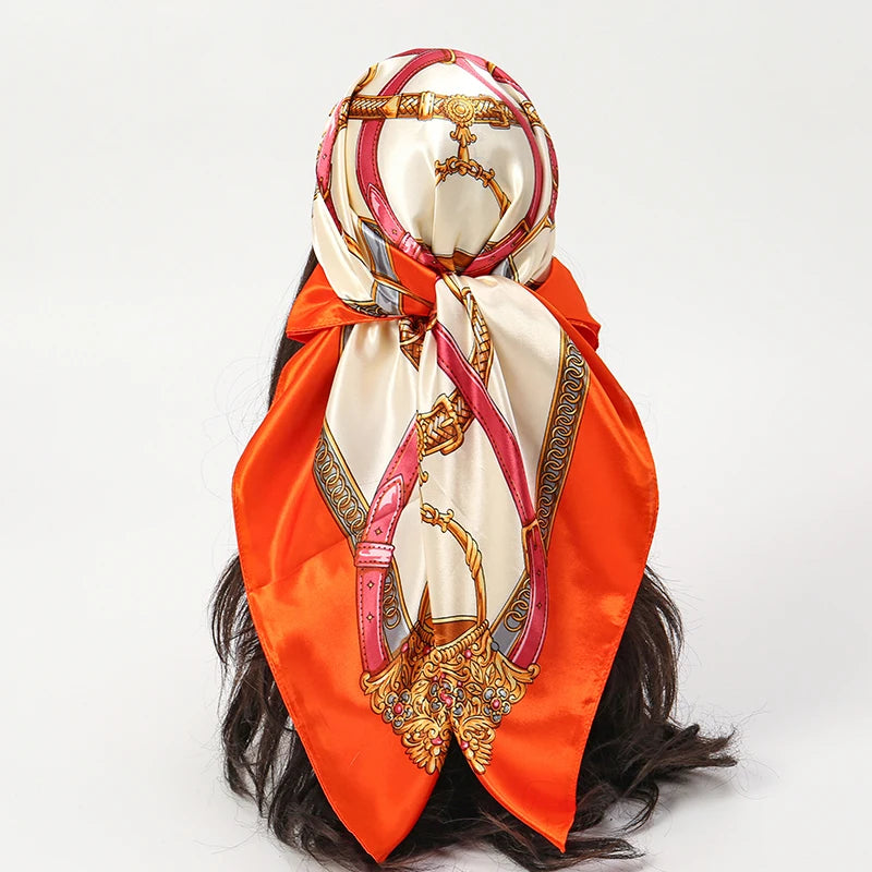 An elegant satin square scarf featuring a pink and gold ornate design tied around dark hair.