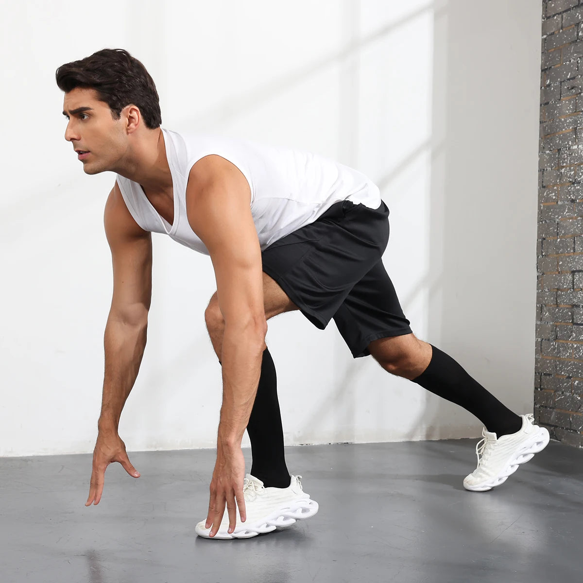 A muscular man wearing black athletic shorts and white compression socks is performing a stretch or exercise.