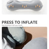 A hand is pressing a portable inflatable camping pillow to inflate it for neck and lumbar support.