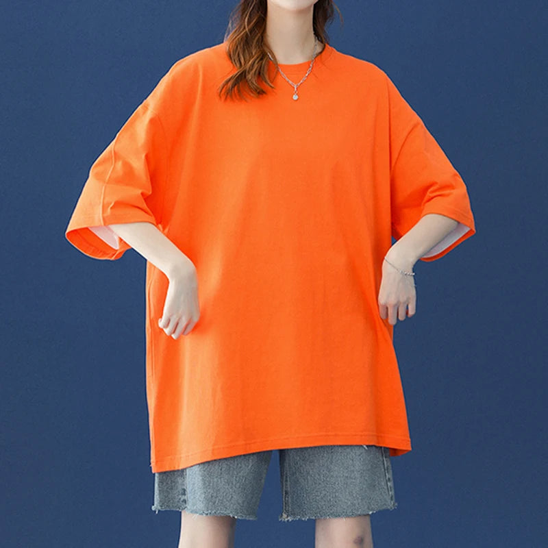 Eine Frau in einem orangefarbenen, oversized Baumwoll-T-Shirt und Jeansshorts vor einem dunkelblauen Hintergrund.