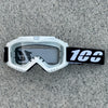 White heavy-duty motorcycle and ATV goggles with a black strap resting on a gray surface.