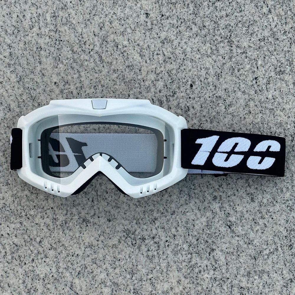 White heavy-duty motorcycle and ATV goggles with a black strap resting on a gray surface.