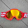 Une paire de lunettes de moto tout-terrain rouges avec des verres réfléchissants posées sur une surface grise.