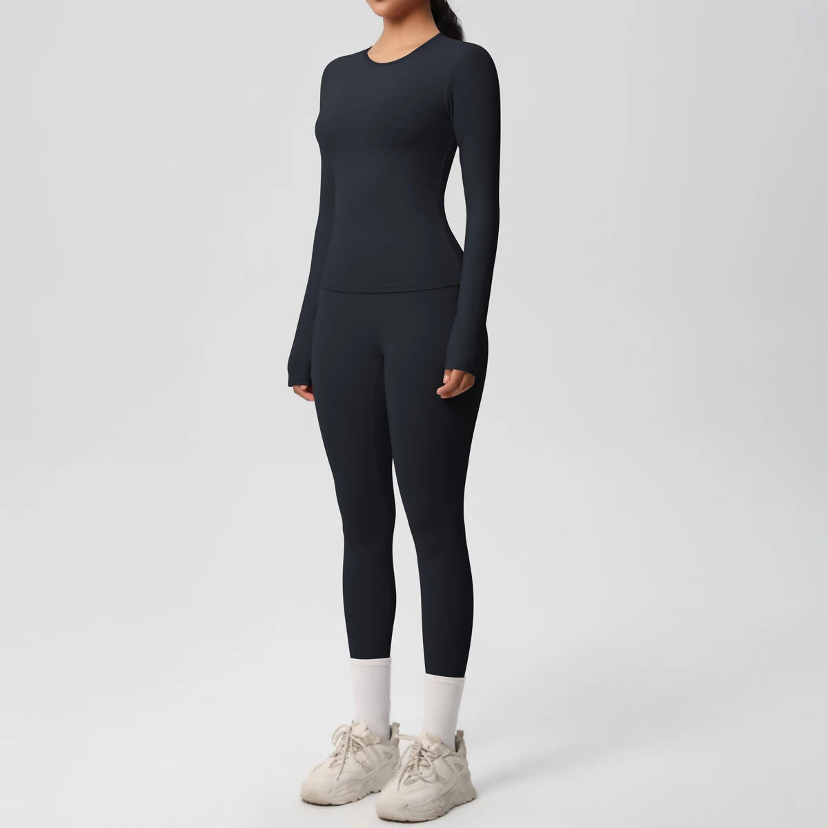 A woman wearing a navy blue long-sleeved top and matching leggings with white socks and light-colored athletic shoes.