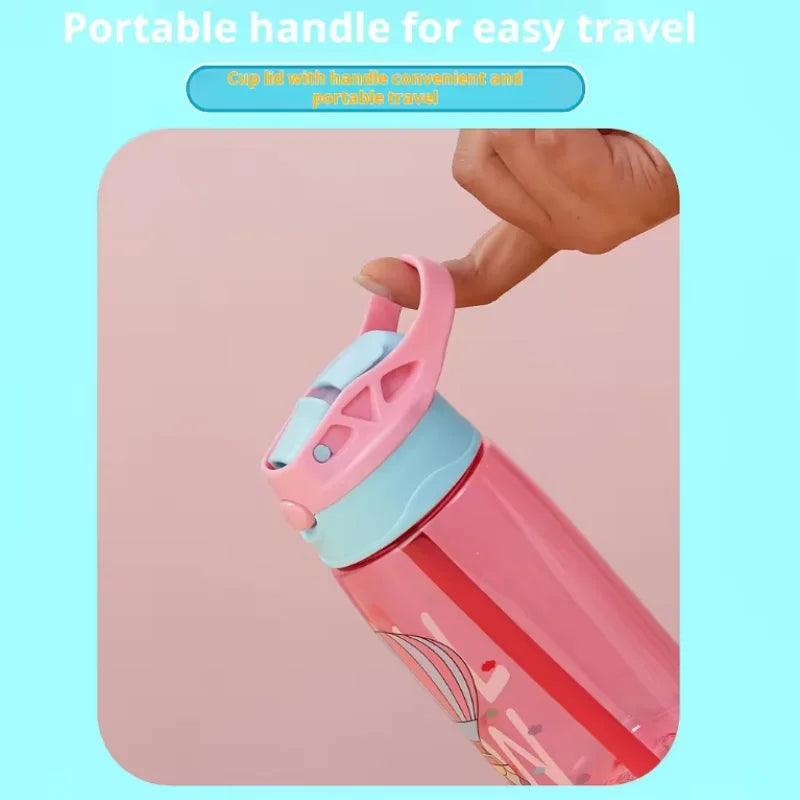 A hand is holding a pink cartoon straw sippy water bottle with a portable handle for easy travel.