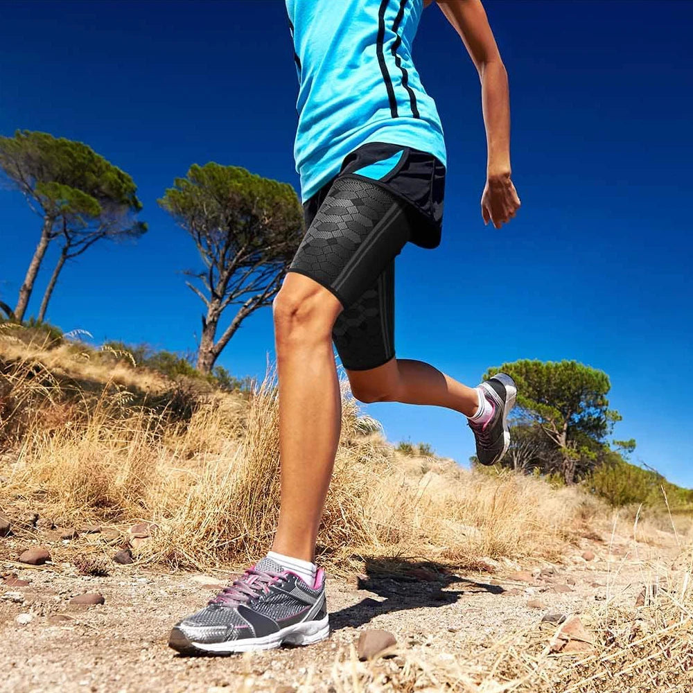 A person running outdoors wearing black compression thigh sleeves and a bright blue shirt.