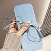 A hand is holding a pair of light blue anti-blue light reading glasses resting on a light blue pad.
