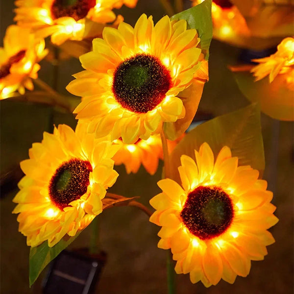 Three bright yellow solar sunflower LED lights blooming on green leaves.
