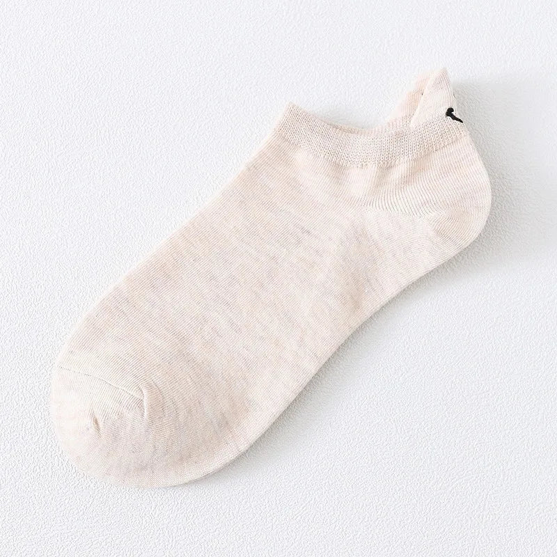 Un par de calcetines de tobillo beige claro con un pequeño bordado de cara sonriente negra.