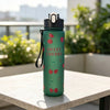 A green reusable water bottle with a sweet cherry design sitting on a light-colored table outdoors.