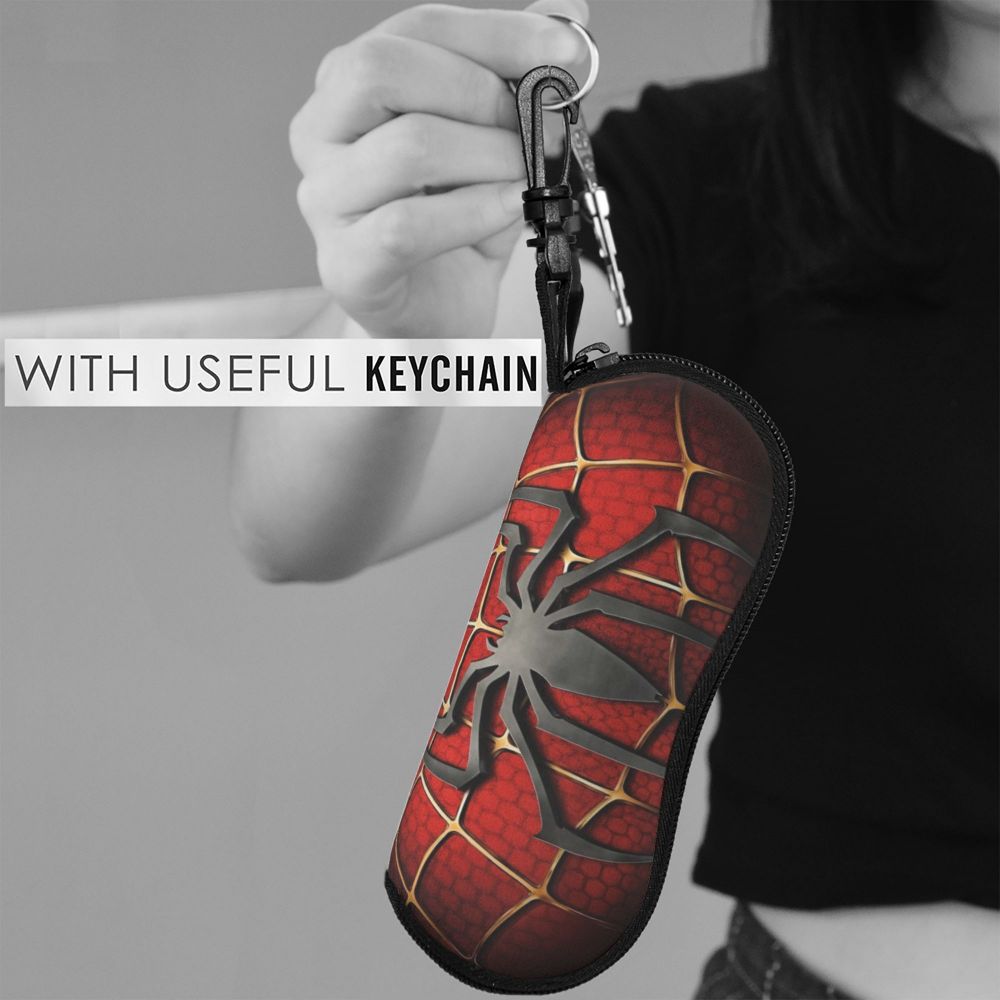 A hand holds a red and black spider web-patterned keychain pouch with a metal clasp.