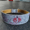 A beige leather weightlifting belt decorated with a white and pink floral pattern and a red sword design.