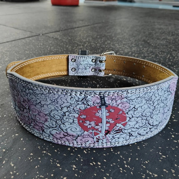 A beige leather weightlifting belt decorated with a white and pink floral pattern and a red sword design.