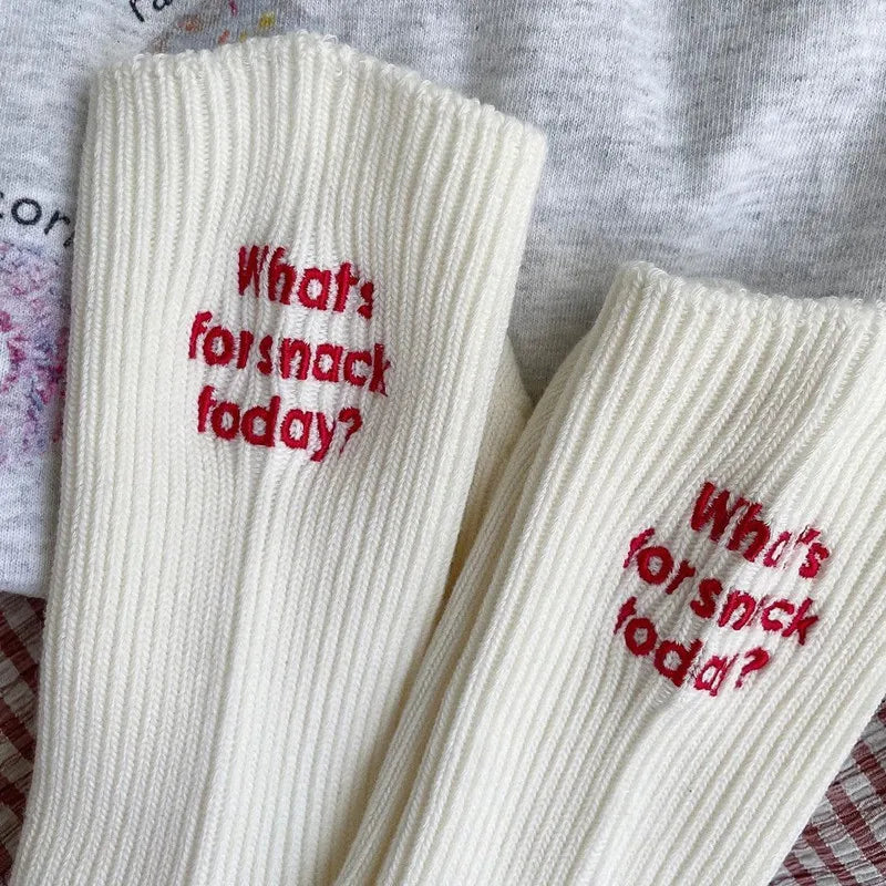 White ribbed cotton socks with red embroidery that reads What's for snack today?