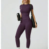 Eine Frau modelliert ein lila Zweiteiler-Yoga-Set mit hohen Bund-Leggings und einem kurzärmeligen Oberteil mit schwarzem Träg