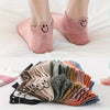 Eight pairs of low-cut ankle socks with smiling embroidery in various muted colors stacked on a white surface.