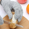 A hand wearing knitted protection gloves is shown cutting a piece of fruit on a wooden board.