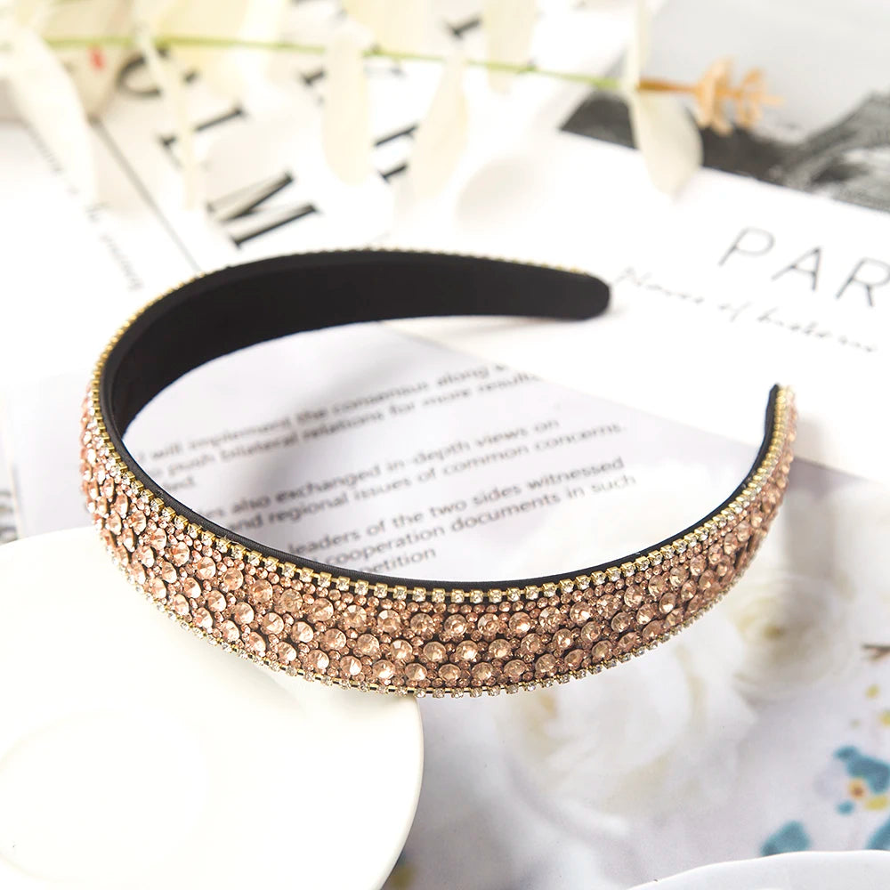 Nahaufnahme eines schwarzen Kristall-Strass-Haarschmucks auf weißem Untergrund mit verschwommenen Blumenmotiven.