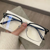 A pair of black and blue-framed retro square eyeglasses resting on a white paper against a gray surface.