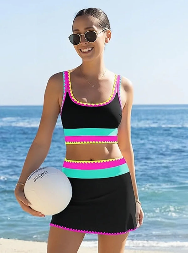 A woman models a black and neon color-block zigzag three-piece swimsuit set outdoors near the ocean.