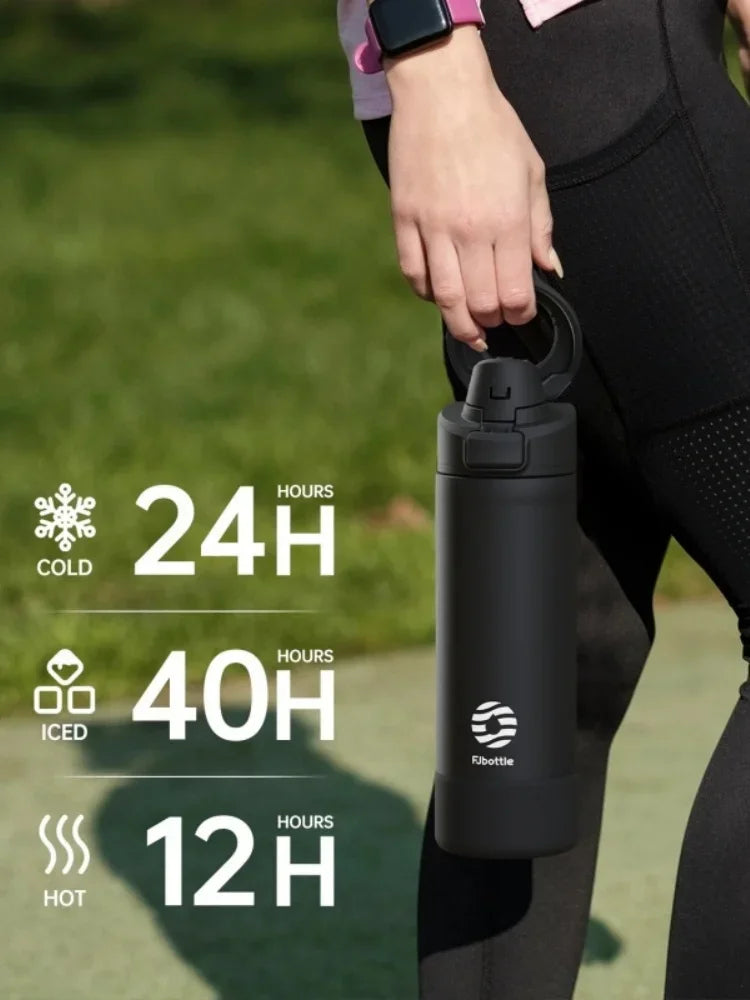 A black insulated sports water bottle with a magnetic lid is held by a person outdoors.