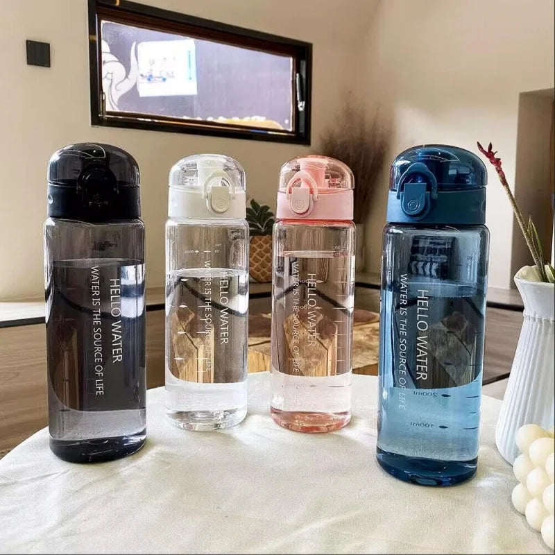 A row of five clear sports water bottles with different colored caps lined up on a white table.