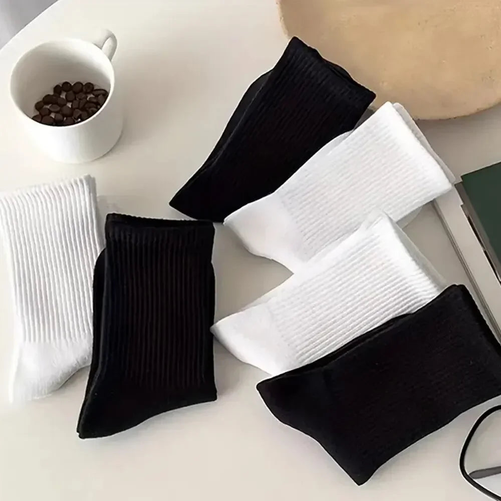 Une collection de chaussettes en tricot respirantes noir et blanc sont exposées sur une surface blanche.
