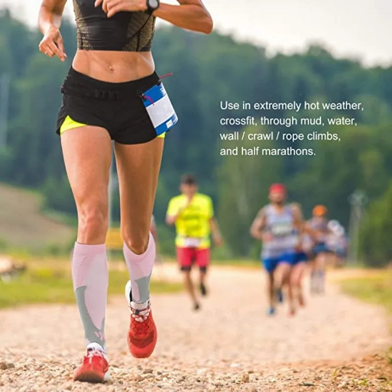 A runner wearing compression socks is jogging on a dirt path in a wooded area.