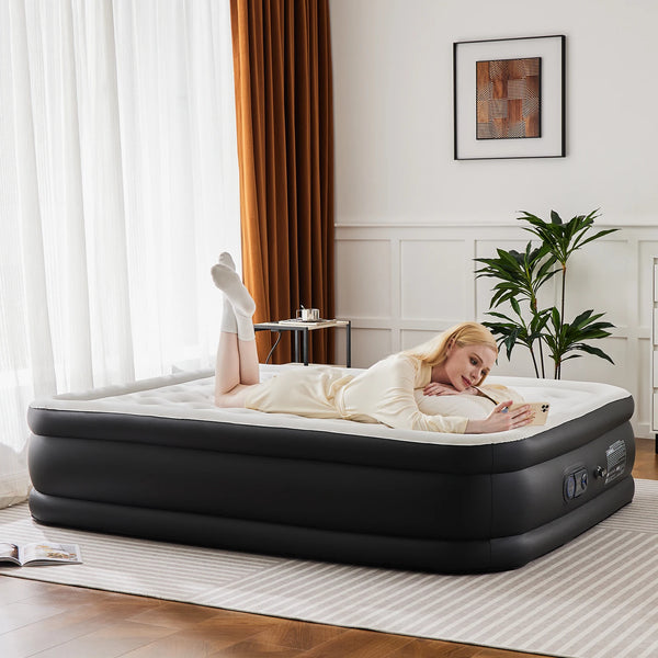 A woman is lying on a black air mattress in a bright room next to a window.