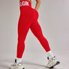 Eine Frau trägt rote, hoch taillierte, nahtlose Yoga-Leggings und ein weißes Sport-BH in einem Studio.