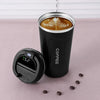A black insulated thermos bottle with a lid and a coffee cup inside, sitting on a pink surface with coffee beans.
