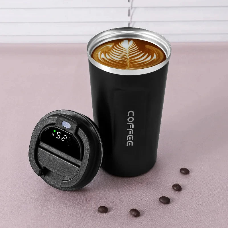 A black insulated thermos bottle with a lid and a coffee cup inside, sitting on a pink surface with coffee beans.